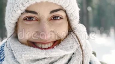 穿着羊毛帽、戴着长长的暖围巾的美丽微笑的女子在雪地冬季公园的模糊的极端特写镜头
